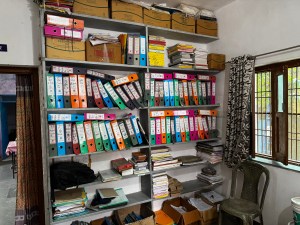 A filing cabinet with shelves containing binders of files, a window on one side, a doorway on the other side.